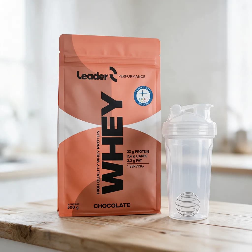 Leader Performance Whey Chocolate -pussi puisella pöydällä shakerin vieressä