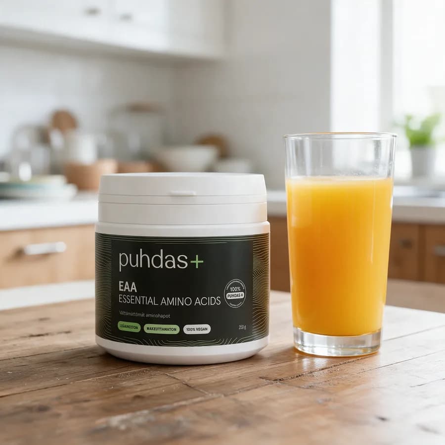 Tummanvihreä Puhdas+ EAA Essential Amino Acids -purkki valkoisella kannella puisella keittiön pöydällä mehulasin vieressä