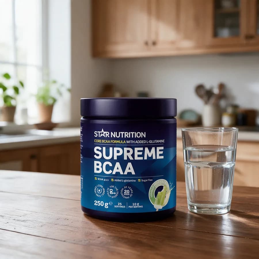 Tummansininen Star Nutrition Supreme BCAA -purkki puisella keittiön pöydällä vesilasin vieressä