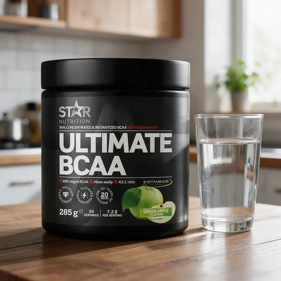 Musta Star Nutrition Ultimate BCAA -purkki vihreällä omenalla puisella keittiön pöydällä vesilasin vieressä