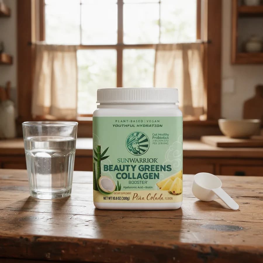 Valkoinen Sunwarrior Beauty Greens Collagen Booster -purkki vaaleanvihreällä etiketillä puisella keittiön pöydällä, vieressä lasi vettä ja mittalusikka